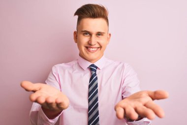 Tişört ve kravat giyen genç yakışıklı iş adamı pembe arka planda dikilip gülümsüyor ve yardım eli uzatıyor ve kabul ediyor..