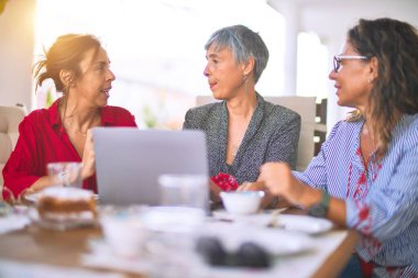 Orta yaşlı kadınlarla buluşup, öğle yemeği yiyip, kahve içiyorlar. Olgun arkadaşlar, güneşli bir günde evde dizüstü bilgisayar kullanarak mutlu bir şekilde gülümserler.