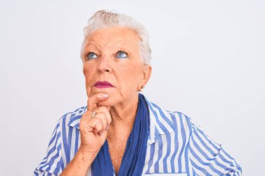 Yaşlı, gri saçlı, mavi çizgili tişörtlü bir kadın izole edilmiş beyaz arka planda dikiliyor. Ciddi bir yüz ifadesi var. Soru sormayı düşünüyor.