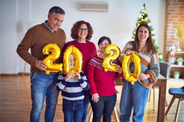 Mutlu ve kendinden emin gülümseyen güzel bir aile. Ayakta durup poz vermek 2020 balonu evde Noel ağacı etrafında kutluyor.