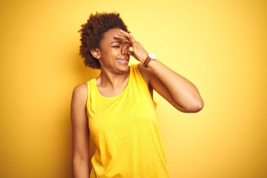 Beauitul Afro-Amerikan kadını izole edilmiş sarı arka plan üzerine yaz tişörtü giyip pis ve iğrenç bir koku kokluyor, nefesini burnunda tutuyor. Kötü koku konsepti.