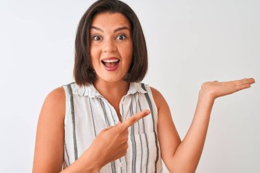 İzole edilmiş beyaz arka planda duran sıradan çizgili tişört giyen genç ve güzel bir kadın mutlu bir şekilde elini ve parmağını işaret ediyor.