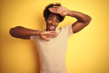 Afro saçlı amerikalı adam çizgili t-shirt izole sarı arka plan üzerinde duran giyen gülümseyen neşeli oynarken elleri yüzünü gösteren bir boo gözetleme. Şaşırttı ve çıktı