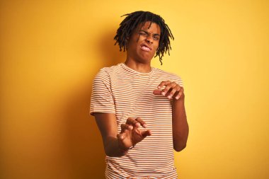 Sarı arkaplanda duran çizgili tişörtlü Afro adam tiksindirici ve tiksindirici bir yüz ifadesi takınıyor çünkü tiksinti tepkisi veriyor. Eller havada. Can sıkıcı bir kavram..