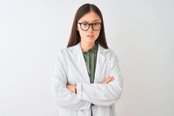 Young chinese scientist woman wearing coat and glasses over isolated white background skeptic and nervous, disapproving expression on face with crossed arms. Negative person.