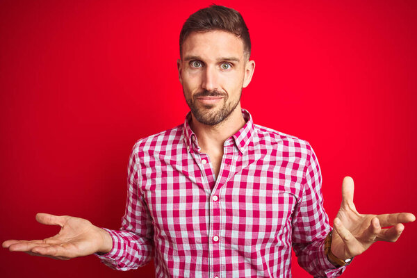 Young handsome man over red isolated background clueless and confused with open arms, no idea concept.