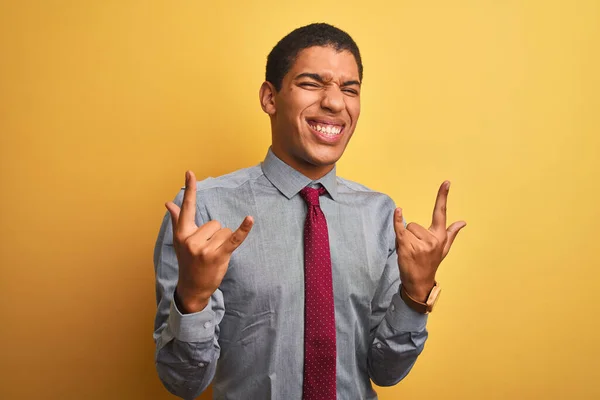 若いハンサムなアラブビジネスマンがシャツを着て 手を上げてロックシンボルをやって狂気の表現で叫んで孤立した黄色の背景にネクタイ 音楽スター 重い概念 — ストック写真
