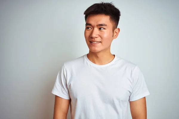 Tシャツを着た若いアジア系中国人男性が白い背景の上に立って笑顔で横を見て 離れて考えて見つめて — ストック写真