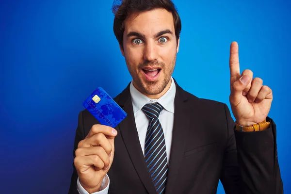 Jovem Empresário Bonito Segurando Cartão Crédito Sobre Fundo Azul Isolado — Fotografia de Stock