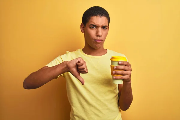 Young handsome arab man drinking take away coffee over isolated yellow background with angry face, negative sign showing dislike with thumbs down, rejection concept