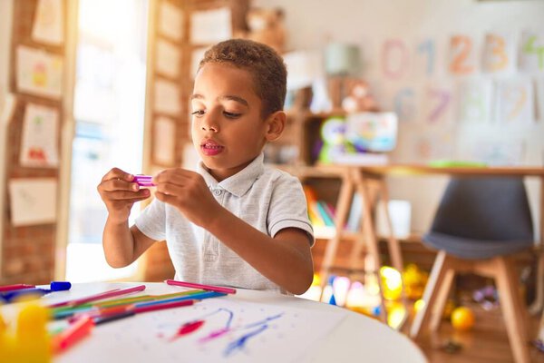 Beautiful african american toddler drawing using paper and marker pen at kindergarten