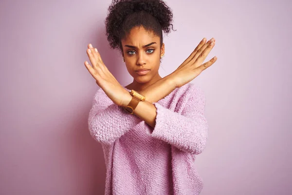 Young african american woman wearing winter sweater standing over isolated pink background Rejection expression crossing arms doing negative sign, angry face