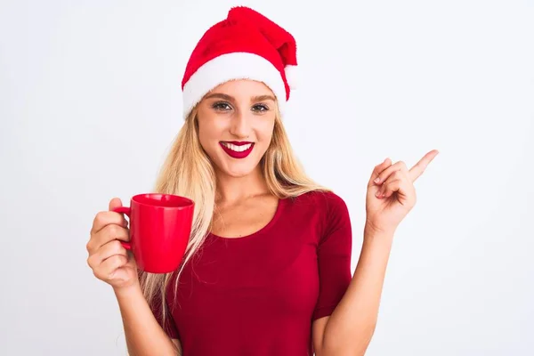 漂亮的女人戴着圣诞圣诞礼帽 站在与世隔绝的白色背景上喝咖啡 手指手画脚 非常高兴 — 图库照片