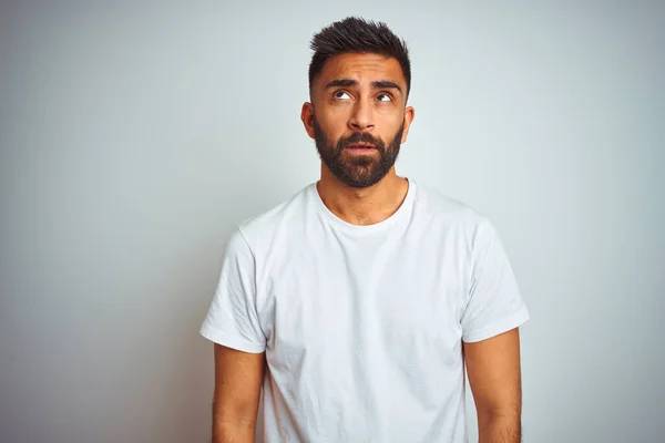 Young indian man wearing t-shirt standing over isolated white background looking sleepy and tired, exhausted for fatigue and hangover, lazy eyes in the morning.