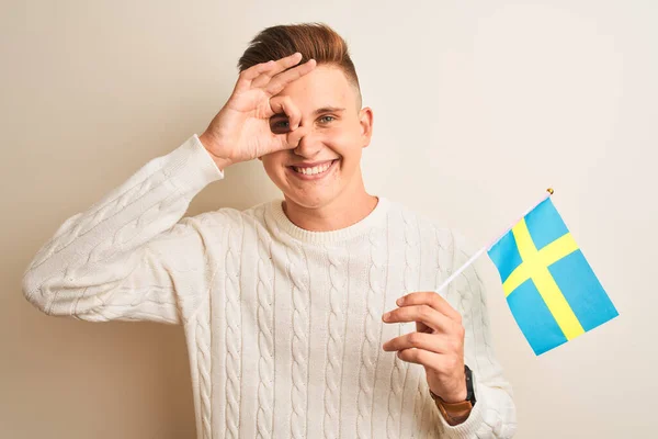 若いですハンサムな男保持スウェーデン語フラグ上の隔離された白い背景とともに幸せな顔笑顔Doing Signとともに手で目を通して指 — ストック写真