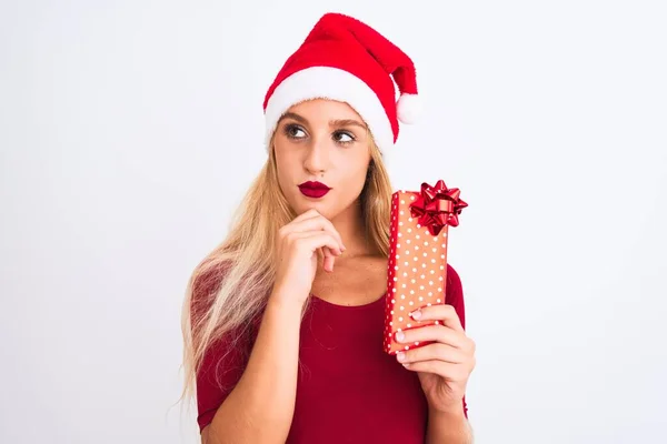 孤立した白い背景深刻な顔の上にギフトを保持クリスマスサンタの帽子を身に着けている美しい女性質問について考えて 非常に混乱したアイデア — ストック写真