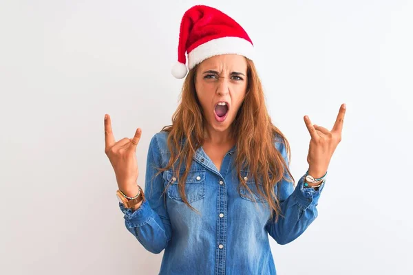 孤立した背景にクリスマスの帽子をかぶっている若い美しい赤毛の女性が手を上げて岩のシンボルをやって狂気の表情で叫んでいます 音楽スター 重い音楽の概念 — ストック写真