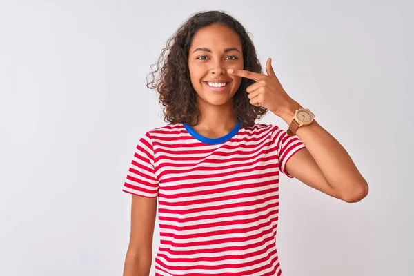 若いブラジル人女性の赤い縞模様のTシャツを着て隔離された白い背景の上に立って顔と鼻に手の指で指して 陽気笑顔 美の概念 — ストック写真