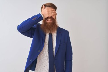 İzole edilmiş beyaz arka planda dikilen takım elbiseli genç kızıl saçlı işadamı. Gülümsüyor ve yüzünde şaşkınlıktan gözleri kapayarak gülüyor. Kör kavram.