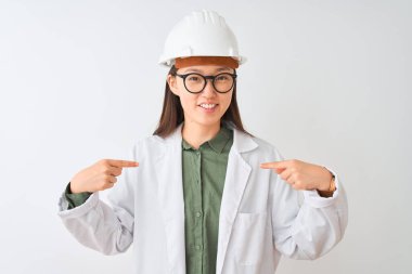 İzole edilmiş beyaz arka planda ceket gözlüğü takan genç Çinli mühendis kadın yüzünde bir gülümsemeyle gururlu ve mutlu bir şekilde kendini işaret ediyor..