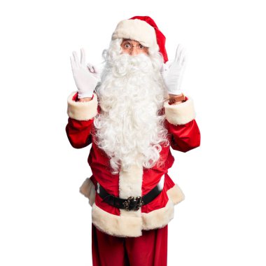 Orta yaşlı yakışıklı adam Noel Baba kostümü ve sakal takmış şaşırmış ve şaşırmış görünüyor. Çılgın ifade