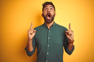 İnzivaya çekilmiş beyaz arka plan üzerinde duran zarif gömlekli genç Hintli işadamı şaşırmış ve şaşırmıştı. Parmaklarıyla işaret ediyor ve kollarını kaldırıyordu..