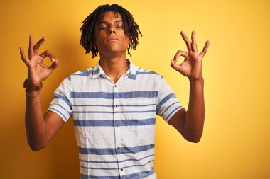 Sarı arka plan üzerinde çizgili tişört giyen Afro-Amerikan adam rahatla ve gözleri kapalı meditasyon hareketi yaparken parmaklarınla gülümse. Yoga konsepti.