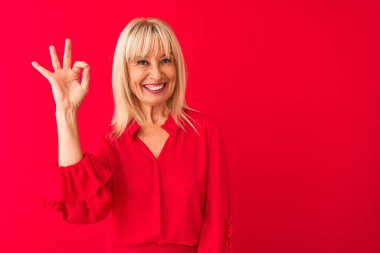 Soyutlanmış kırmızı arka planda duran zarif tişörtlü, orta yaşlı bir kadın el ve parmaklarıyla 