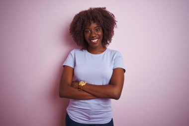 İzole edilmiş pembe arka planda duran, kollarını kavuşturup kameraya bakan, gülümseyen, Afro tişörtlü genç bir kadın. Pozitif kişi.