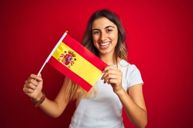 İspanyol bayrağını kırmızı izole arka planda tutan genç ve güzel bir kadın mutlu bir yüzle ayakta duruyor ve kendine güvenen bir gülümsemeyle dişlerini gösteriyor.