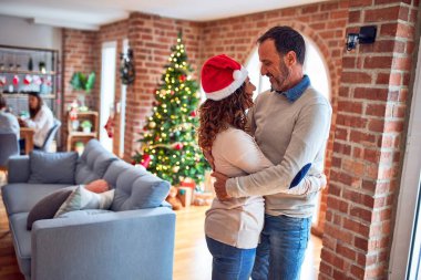 Orta yaşlı güzel çift mutlu ve kendinden emin gülümsüyor. Evde Noel ağacının etrafında dikilip sarılıyorsun.