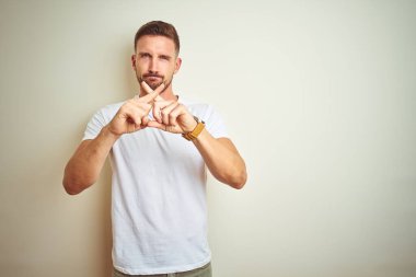 Eksi işareti yapıyor izole arka plan ret ifade geçiş parmakları üzerinde rahat beyaz t-shirt giyen genç yakışıklı adam