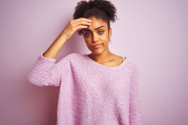 Kışlık kazak giyen genç Afro-Amerikalı kadın pembe arka planda duruyor. Alnındaki sorun yüzünden endişeli ve stresli. Kriz konusunda endişeli.