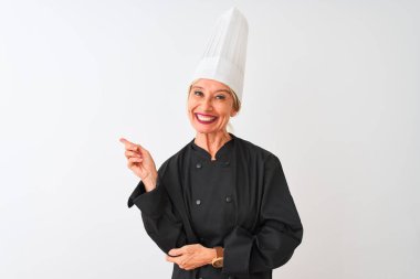 Üniformalı ve şapkalı orta yaşlı bir aşçı kadın izole edilmiş beyaz arka planda duruyor. Yüzünde kocaman bir gülümseme var. Elleri ve parmakları kameraya bakıyor..