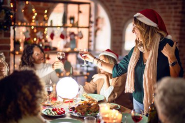 Mutlu ve kendinden emin gülümseyen güzel bir kadın grubu. Her birinin elinde şarap bardağıyla evde Noel 'i kutlayan konuşmaları var.