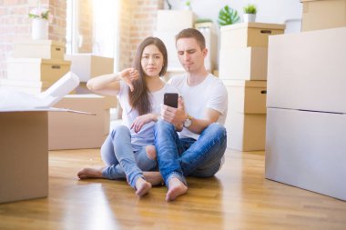 Güzel bir çift yeni evinde, kızgın yüzlü karton kutuların etrafında akıllı telefon kullanıyor. Negatif işaretler baş parmakları aşağıda, reddedilme kavramından hoşlanmadıklarını gösteriyor.