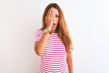 Genç kızıl saçlı kadın, çizgili günlük tişört giyiyor, beyaz tenha arka planda batıyor, bir gözünü eliyle kapatıyor, yüzünde kendine güvenen bir gülümseme ve sürpriz bir duygu var..