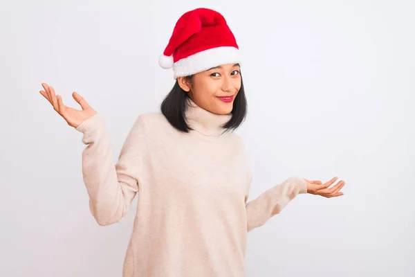 隔離された白い背景にクリスマスのサンタの帽子を身に着けている若い美しい中国の女性は腕と手との混乱した表現を上げました 疑いの概念 — ストック写真