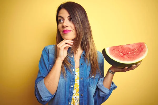 年轻美丽的女人吃着新鲜健康的西瓜片在黄色的背景下严肃地思考着问题 非常迷惑的想法 — 图库照片
