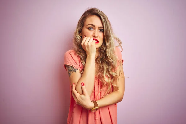 年轻的漂亮女人穿着T恤站在粉红色的孤立背景看起来紧张和紧张与手的嘴咬指甲 焦虑问题 — 图库照片