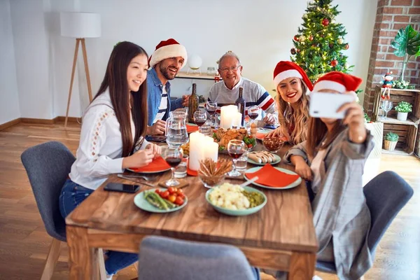 美丽的家庭戴着圣诞礼帽 面带微笑 快乐而自信 在家里吃烤火鸡 用智能手机庆祝圣诞节 — 图库照片