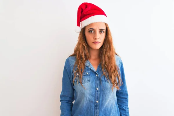 孤立した背景にクリスマスの帽子をかぶっている若い美しい赤毛の女性顔に深刻な表情でリラックスしてください シンプルで自然なカメラを見て — ストック写真