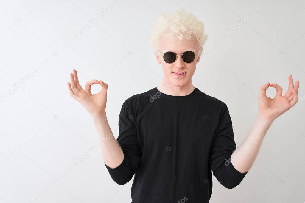 Young albino man wearing black t-shirt and sunglasess standing over isolated white background relax and smiling with eyes closed doing meditation gesture with fingers. Yoga concept.