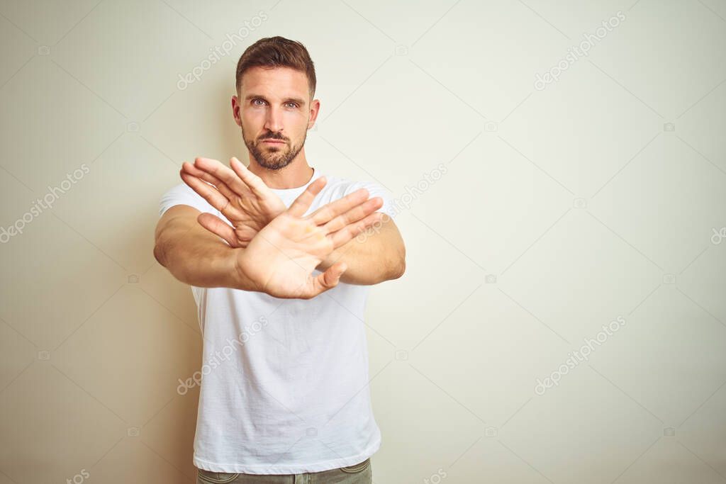 Young handsome man wearing casual white t-shirt over isolated background Rejection expression crossing arms and palms doing negative sign, angry face