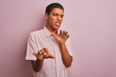 Genç, yakışıklı, sıradan bir gömlek giyen, pembe arka planda duran, tiksindirici, tiksindirici, tiksindirici bir yüz ifadesi takınan Arap bir adam. Eller havada. Can sıkıcı bir kavram..