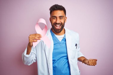 Genç Hintli doktor elinde kanserli kurdele, pembe arka planda durmuş gururla bağırıyor ve zaferi ve başarıyı kutluyor.