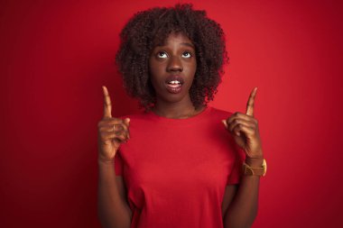 Genç Afrikalı Afro kadın tişört giyiyordu. Kırmızı arka plan üzerinde duruyordu. Şaşırmış ve şaşırmıştı..