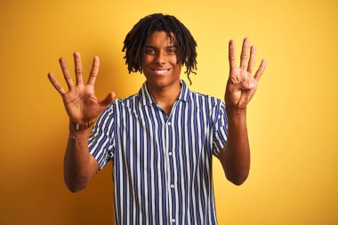 Rastgele çizgili tişört giyen Afro adam izole edilmiş sarı arka plan üzerinde dokuz numarayı gösterirken kendine güvenen ve mutlu bir şekilde gülümseyen.