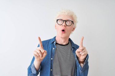 Genç albino sarışın adam kot gömlek ve gözlük takıyor. İzole edilmiş beyaz arka planda şaşkın şaşkın bakıyor, parmaklarıyla işaret ediyor ve kollarını kaldırıyordu..