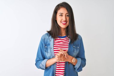 İzole edilmiş beyaz arka plan üzerine çizgili t-shirt ve kot gömlek giyen genç Çinli kadın ellerini birleştirip gülümseyerek gevşemiş ve neşeli gülümsüyor. Başarı ve iyimser